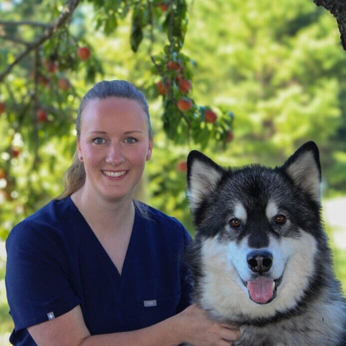 A woman standing next to a dog in front of some trees.