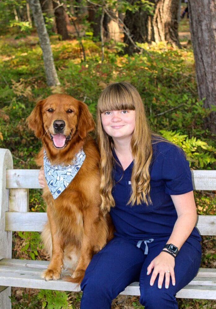 A woman sitting on the back of a bench with her dog.