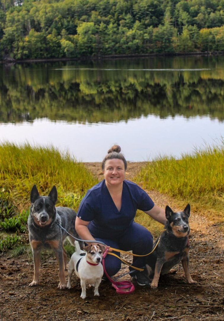 A woman kneeling down with two dogs on the ground.